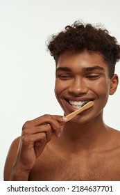 Partial Of Smiling Black Guy Brushing His Teeth With Toothpaste. Young Slim Brunette Curly Man With Naked Torso. Dental Care And Hygiene. Isolated On White Background. Studio Shoot