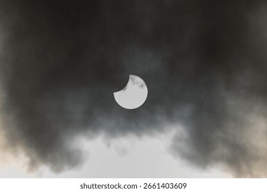 A partial solar eclipse occurs as the moon obscures part of the sun, surrounded by dynamic cloud formations. The event takes place in the daytime, providing a stunning visual experience. Europe. - Powered by Shutterstock - Get 15% off with code: PIKWIZARD15