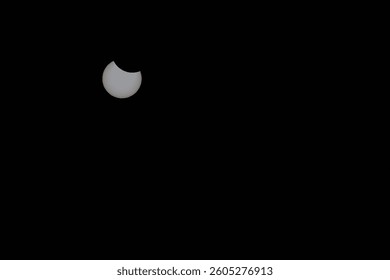 A partial solar eclipse on March 29, 2025, is visible in the sky at noon, forming a crescent against a dark background. Sunspots and coronal flares are visible. Taken in Kollund, Denmark.