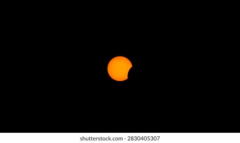 Partial solar eclipse with orange sun and lunar silhouette against black sky