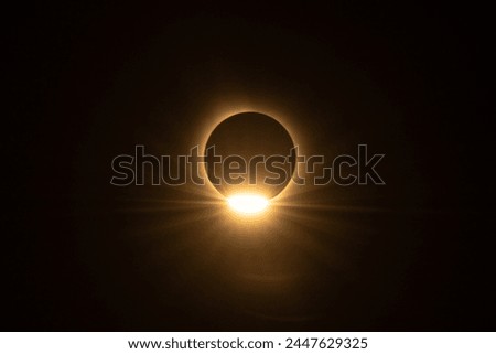 Partial solar eclipse of the sun. Sun peeking through past the moon during the solar eclipse in 2024 presenting a glowing warm aura.