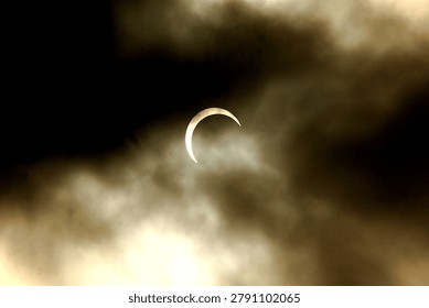 Partial solar eclipse visible through dark atmospheric clouds creating a dramatic celestial scene in the sky. Natural astronomical phenomenon captured outdoors during daytime.
