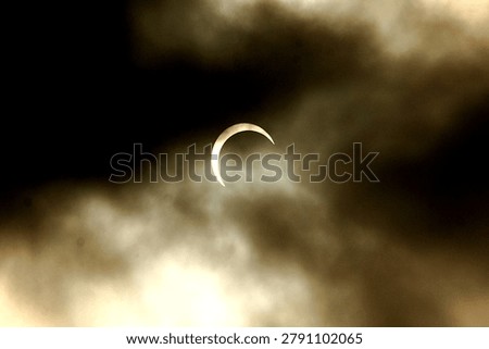 Partial solar eclipse visible through dark atmospheric clouds creating a dramatic celestial scene in the sky. Natural astronomical phenomenon captured outdoors during daytime.
