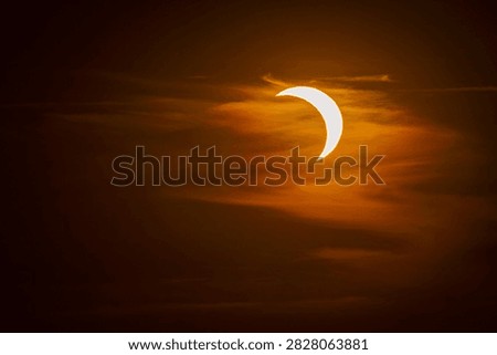 Partial solar eclipse visible through dramatic, dark orange clouds. Crescent sun partially covered by the Moon during an astronomical event. Dark moody sky, space phenomena, and fiery atmosphere.