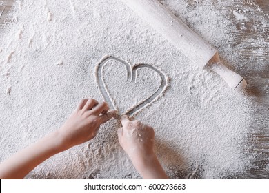 'Partial top view of child drawing heart symbol in flour on table, Mothers day concept