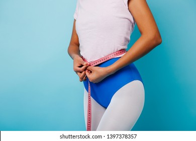 Partial view of african woman measuring waist. Studio shot of fit black girl with measure tape posing on blue background.