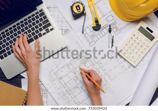 partial view of architect working on blueprints at\
workplace with laptop
