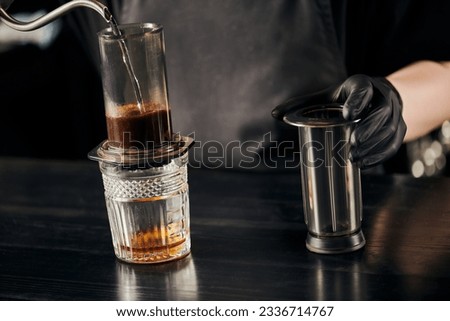 partial view of barista pouring boiling water in aero press coffee maker, alternative espresso method