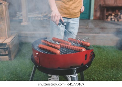 partial view of boy cooking hot dog sausages on grill