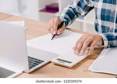 partial view of businessman making calculations at workplace with documents and laptop - Shutterstock ID 1225335574