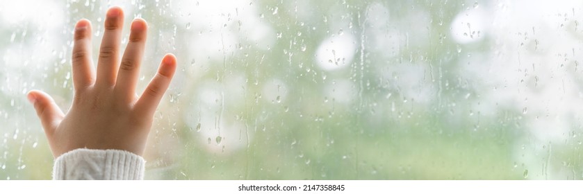 partial view of child touching wet window glass, banner
