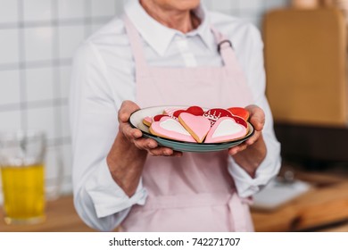 partial view of coffee shop worker holding plate with cookies