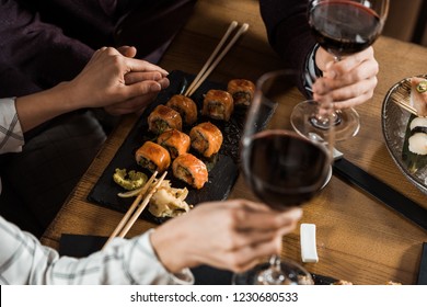Partial view of couple holding hands while drinking wine and eating sushi in restaurant