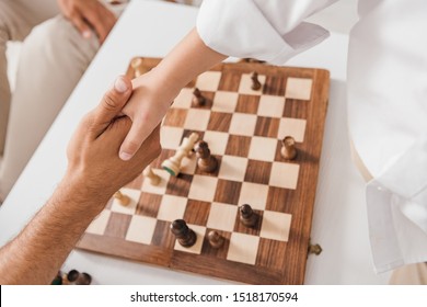 partial view of dad and son shaking hands over chessboard 