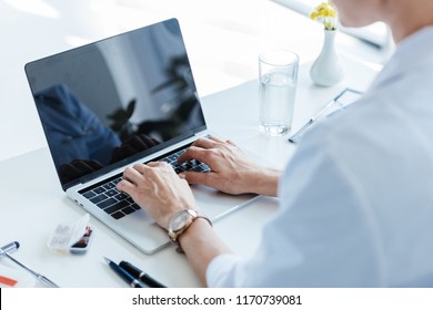 Partial View Of Female Doctor Typing On Laptop With Blank Screen At Table In Office 