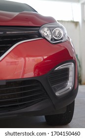 Partial view of the front grille and headlight of a ruby red car.