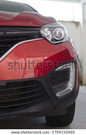 Partial view of the front grille and headlight of a ruby red car.
