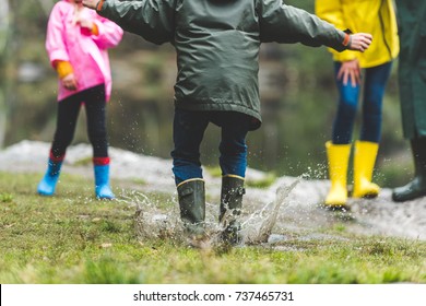 Partial View Of Kid In Raincoat And Rubber Boots Jumping In Muddy Puddle In Autumn Forest