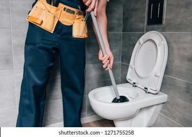 partial view of male plumber using plunger and cleaning toilet in bathroom 