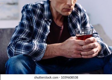 partial view of man with alcohol drink sitting on sofa at home