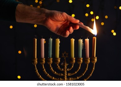 partial view of man lighting up candles in menorah on black background with bokeh lights on Hanukkah