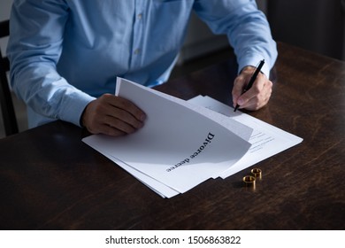 partial view of man sitting at table and signing divorce documents