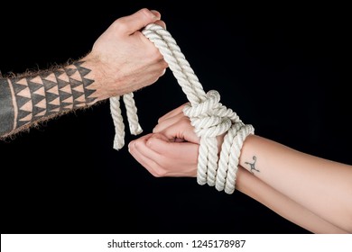 partial view of man tying rope on female hands with tattoo isolated on black