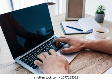 partial view of man typing on laptop at table with coffee cup, textbook, photo frame and potted plant - Shutterstock ID 1097133332