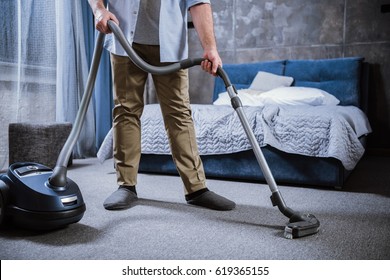 Partial view of man with vacuum cleaner cleaning carpet in bedroom