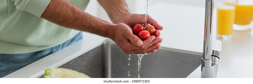 partial view of man washing cheery tomatoes in kitchen, banner - Powered by Shutterstock