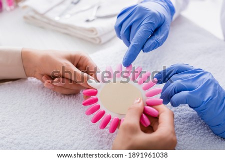 partial view of manicurist pointing with finger at fake nails palette in hands of client