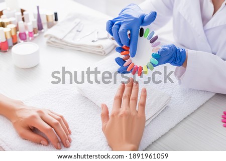 partial view of manicurist pointing with finger at fake nails palette near client