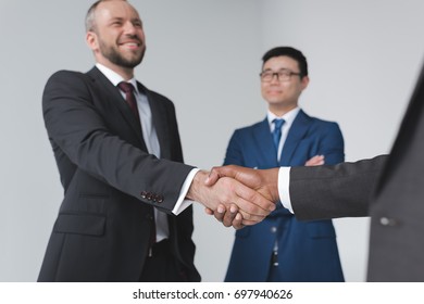 partial view of multicultural businessmen shaking hands after meeting isolated on grey