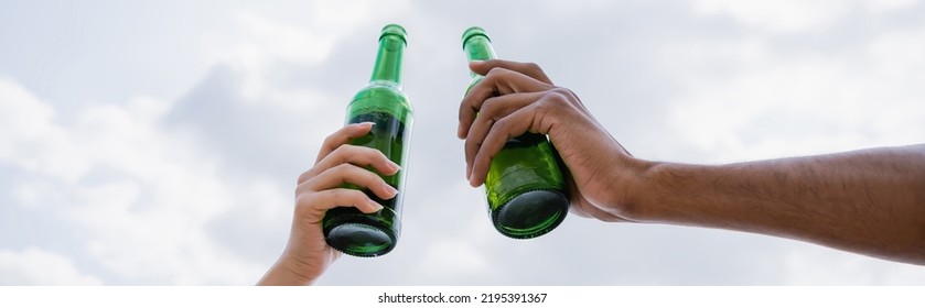 partial view of multicultural friends with beer bottles against cloudy sky, banner