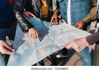 partial view of multiethnic friends pointing at map