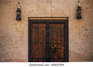 Partial view of an old and grunge wooden door with two petromax hanging lights on both sides.