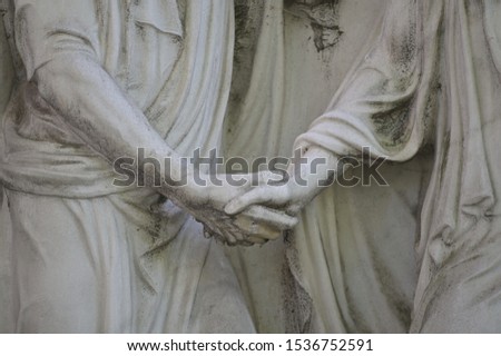 Partial view of an old and weathered sandstone sculpture. A redeeming handshake.