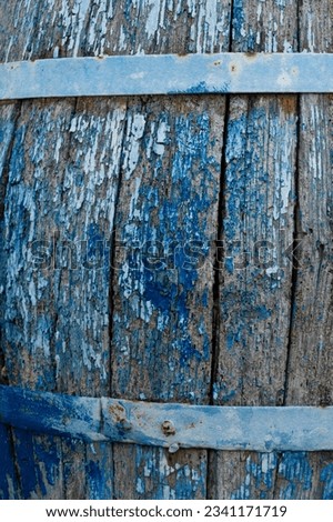 Partial view of an old wooden barrel. Blue tones. Worn paint and rotten wood. Rusty iron bars.