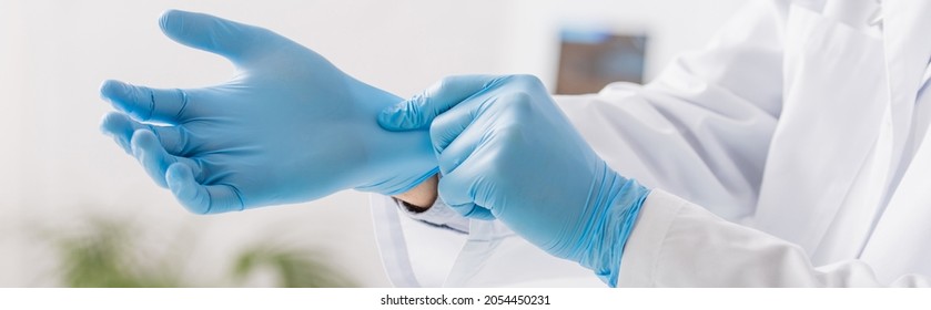 partial view of physician putting on blue latex gloves in clinic, banner