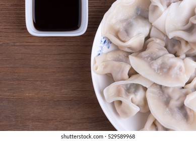 Partial View Of Plate With Steamed Chinese Dumplings (Jiaozi), Soy Sauce, On Wooden Table, Overhead