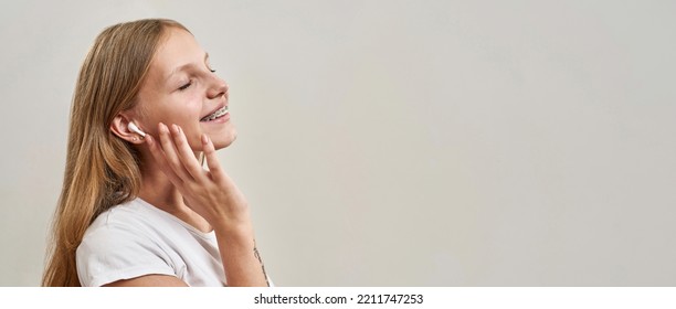 Partial View Of Pleased Caucasian Teenage Girl With Closed Eyes Listening Music In Earphones. Female Child Of Zoomer Generation. Modern Youngster Lifestyle. White Background. Studio Shoot. Copy Space