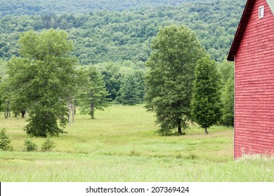 Partial view of a red barn and open field with trees.