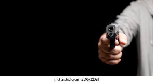 Partial View Of Robber Body Holding Gun In Hand. Close Up Shot Of Modern Firearm Barrel Against A Dark Background. Violent Armed Crimes Or Self Defense Against Thieves Concept.  