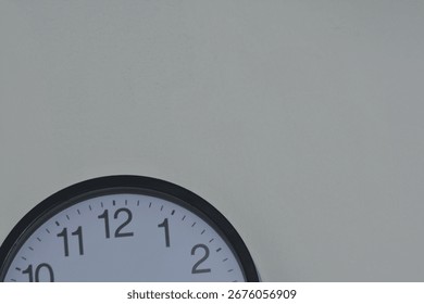 Partial view of round wall clock with black frame and white face against light wall. Clean, minimal design ideal for time, interior, punctuality, and lifestyle themes. Timeless and versatile.