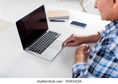 partial view of senior man working on laptop with blank screen at table with notebook at home