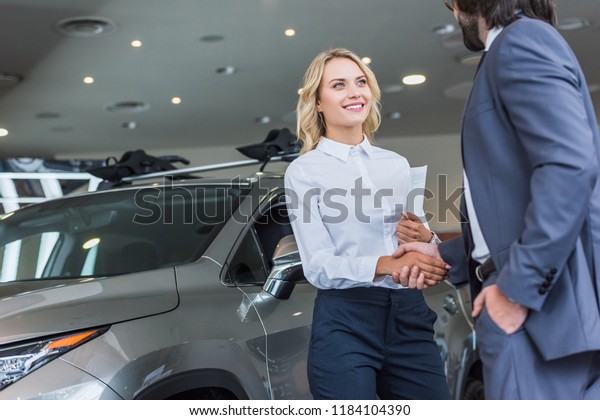 partial view of smiling auto salon\
seller and businessman shaking hands at dealership\
salon