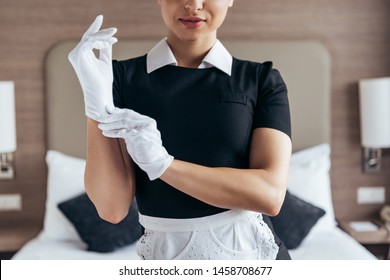 Partial View Of  Smiling Maid In White Apron Putting On Gloves In Hotel Room