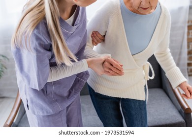 Partial View Of Social Worker Helping Elderly Woman Getting Up From Sofa At Home