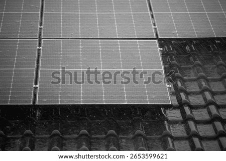 Partial view of solar panels on dark tiled roof during rain.