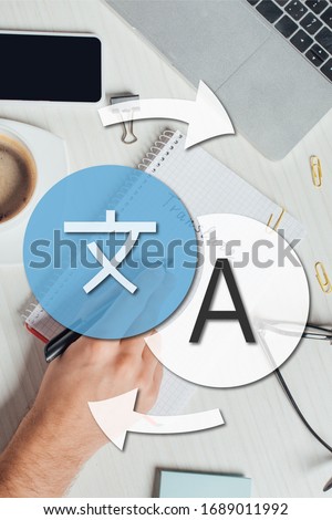 partial view of translator working with notepad, laptop and smartphone on workplace with cup of coffee, translation icon